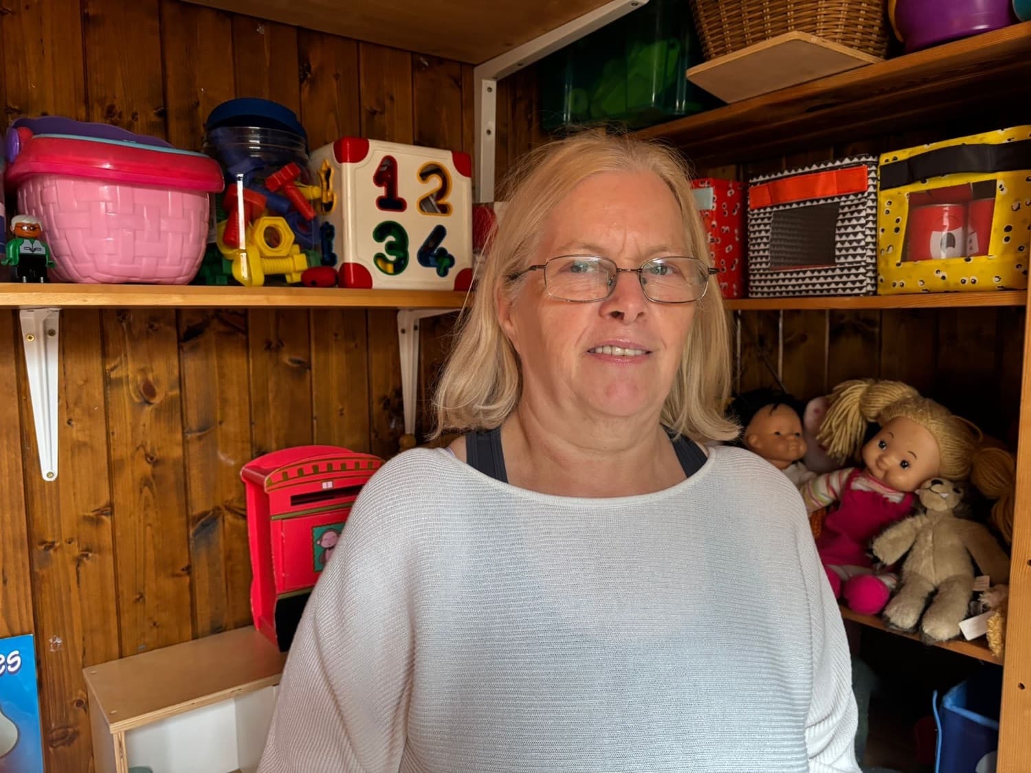 Mary smiling in her playroom, with shelves of toys and dolls behind her
